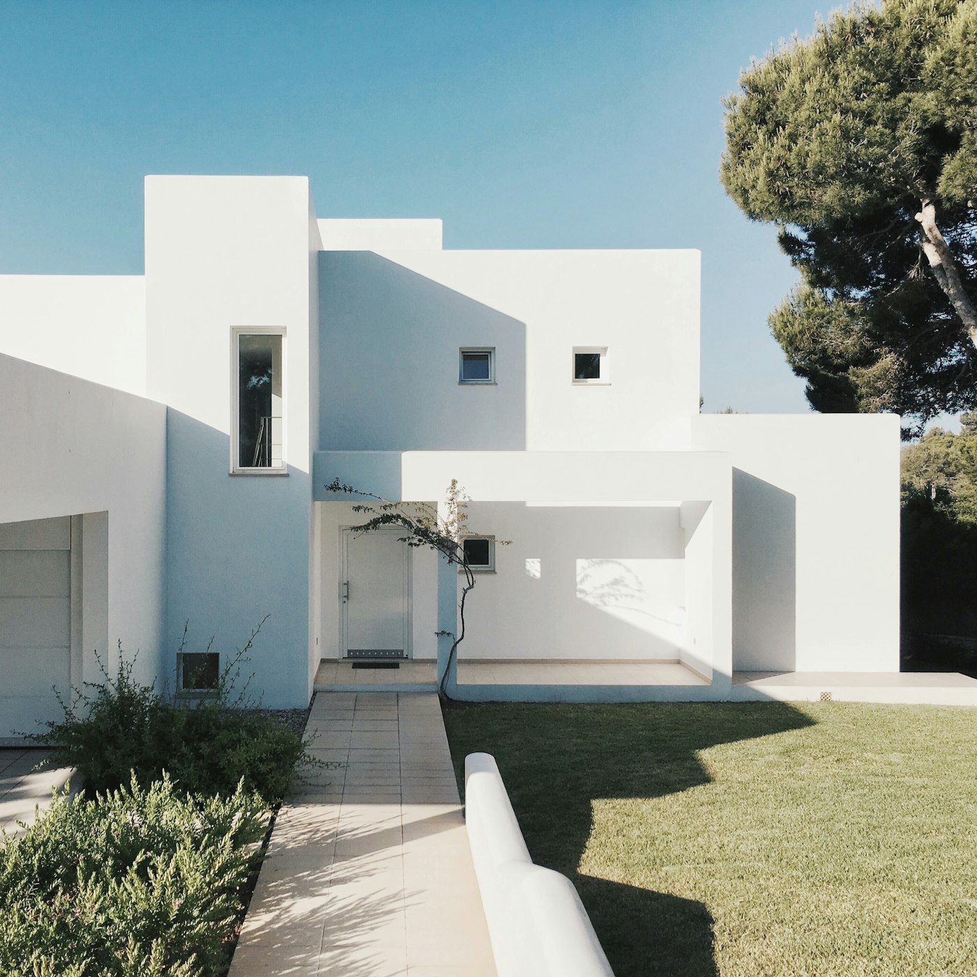 Clean tiled walkway cutting through a manicured lawn to a white modern home